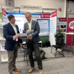 David Payne, Kentegra's Chief Revenue Officer holding a pamphlet that he's viewing together with another gentleman at the 2024 Annual Biocontrol Industry Meeting in Basel, Switzerland